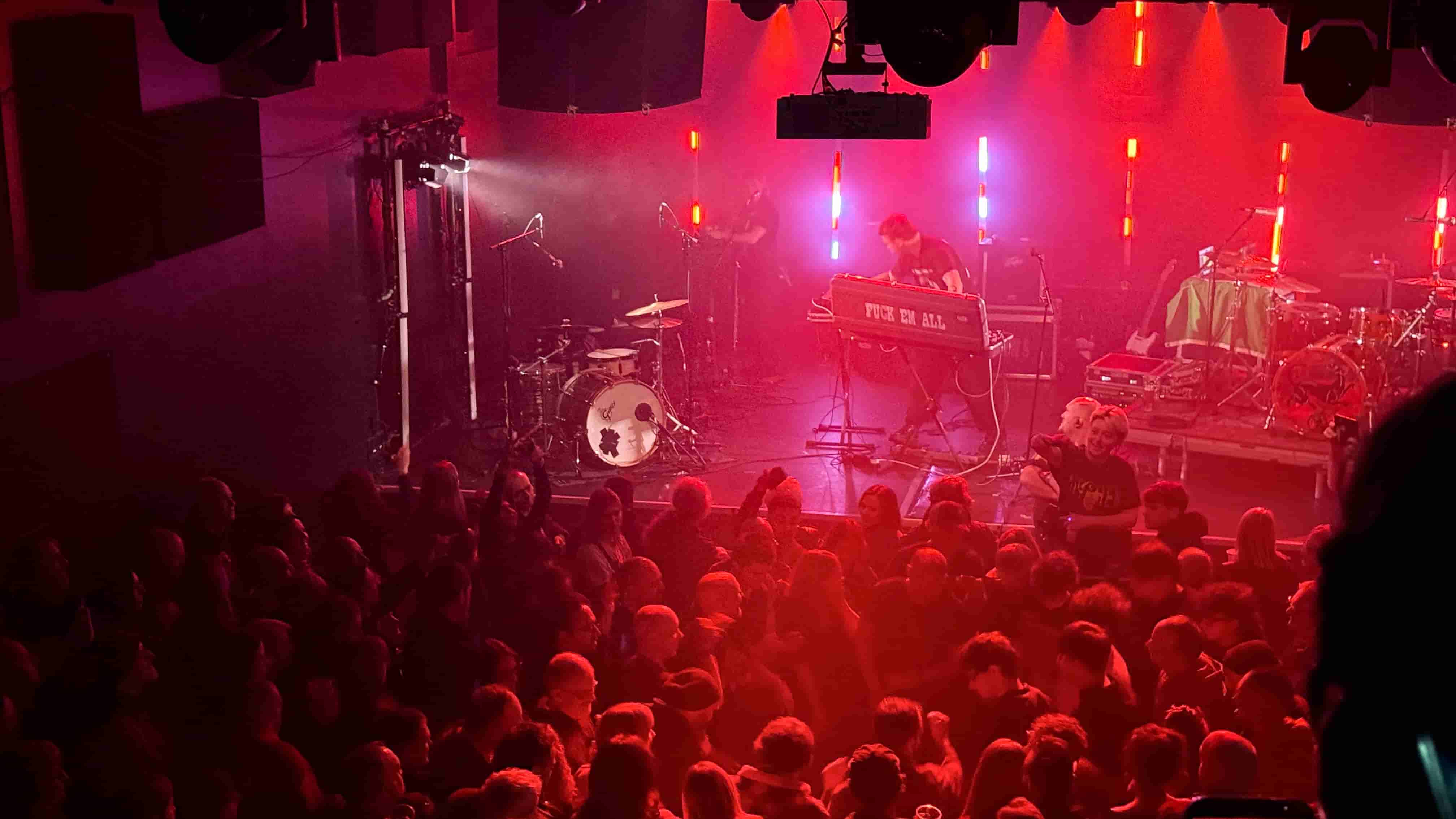 Gans band on stage at the Rescue Rooms Nottingham shot from above the band are bathed in red light. On the left is the drummer, on the right the guitarist and at back the saxophonist
