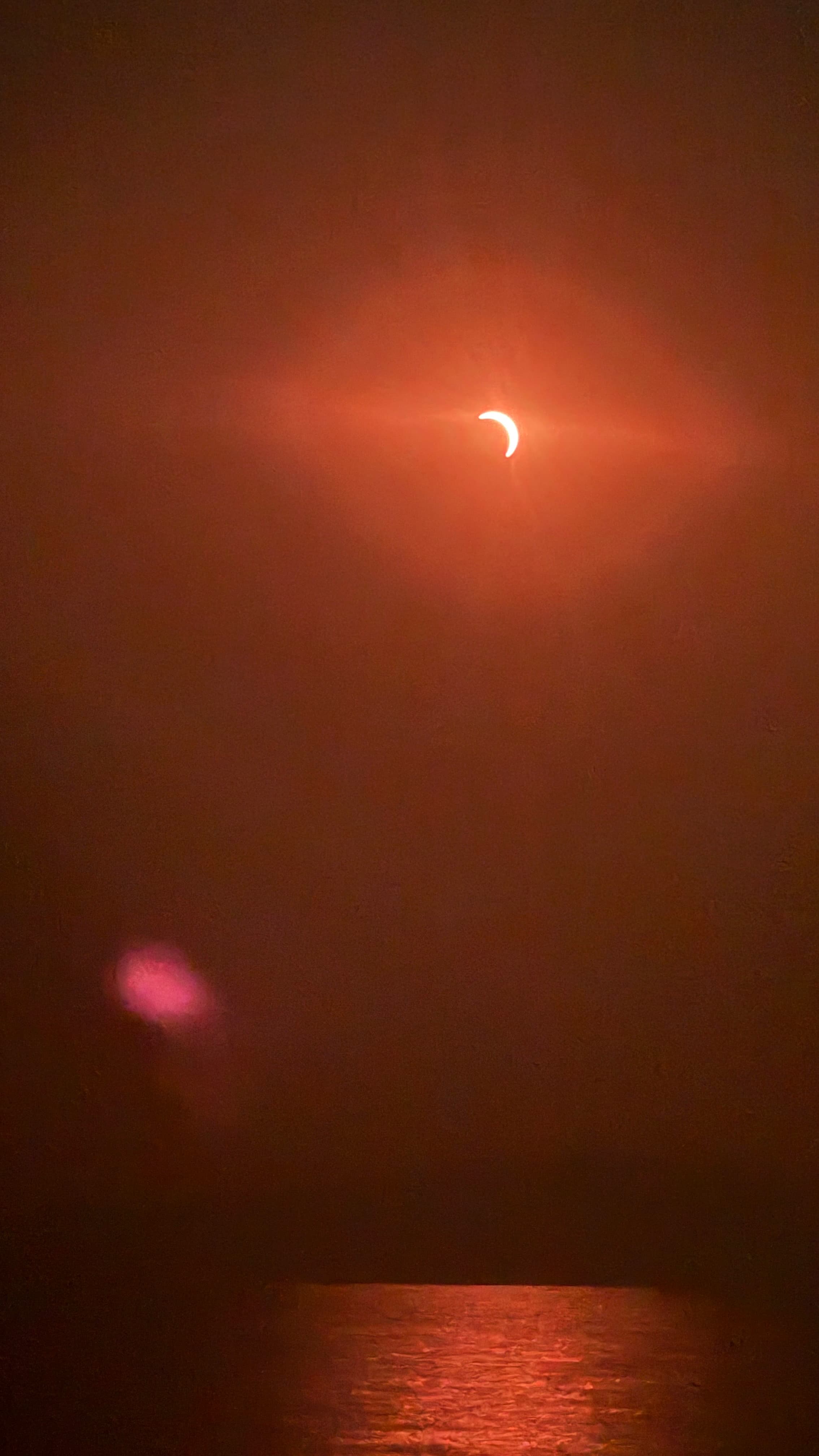 A partial solar eclipse the moon has obscured most of the sun and only a cresent of the top right of the sun is visible below you can see the sea