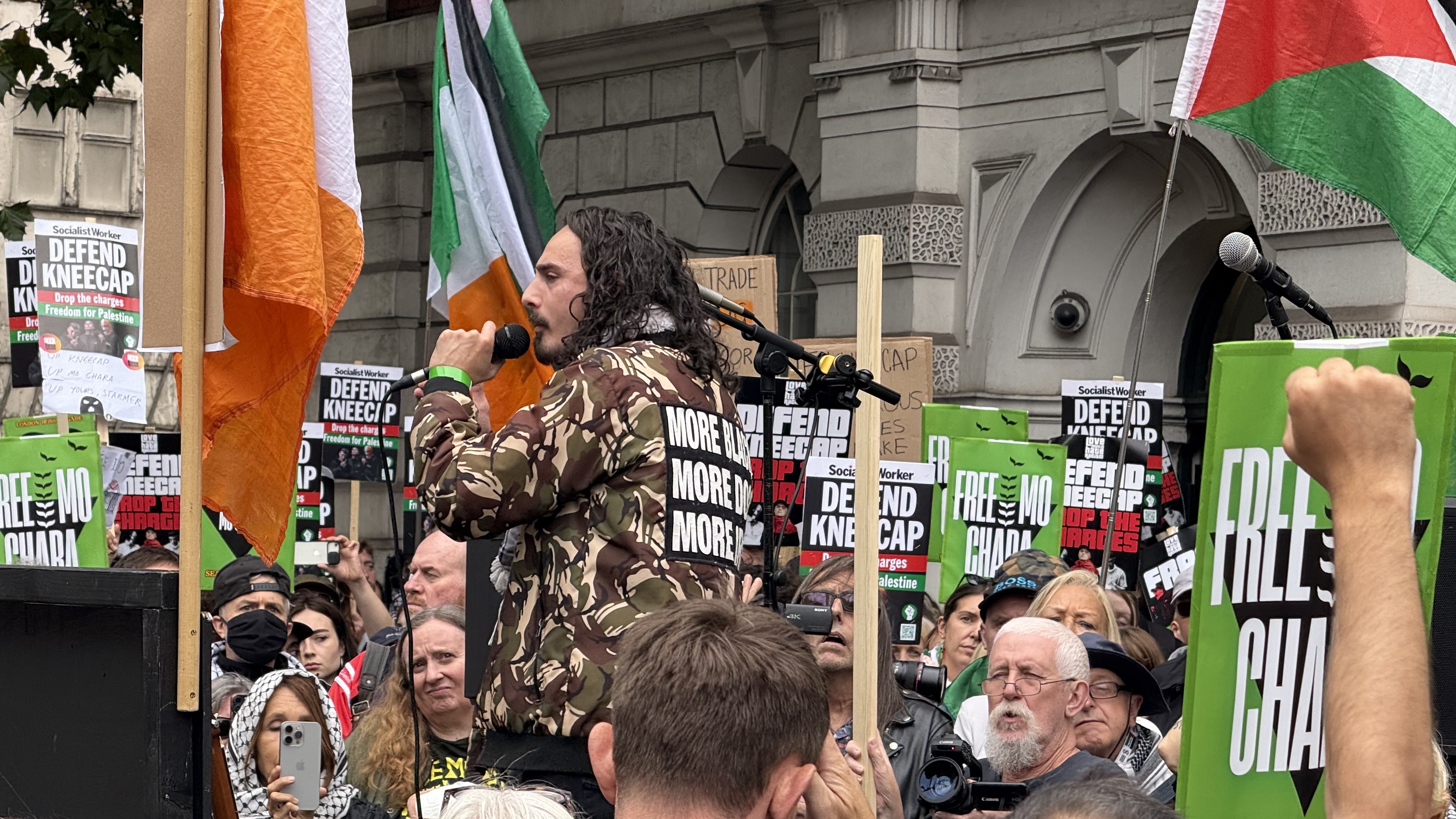 A Palestinian rapper on stage wearing a jacket that reads More blacks More Dog More Irish