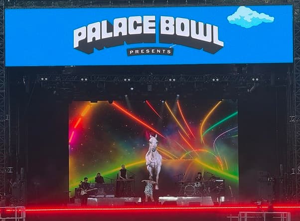 Sophie Ellis Bextor on Stage at Palace Bowl Presents festival, she is where a glittery dress and behind her is a video screen with neon lights and a white horse galloping towards the front