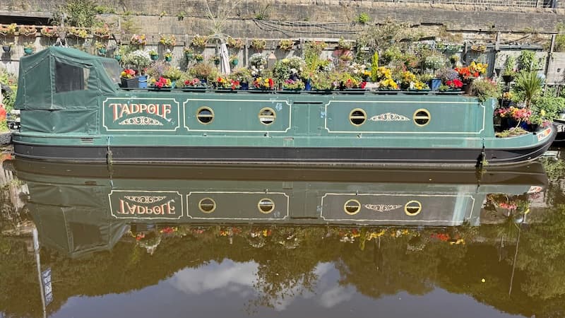 A canal boat covered in flowers reflected in the water