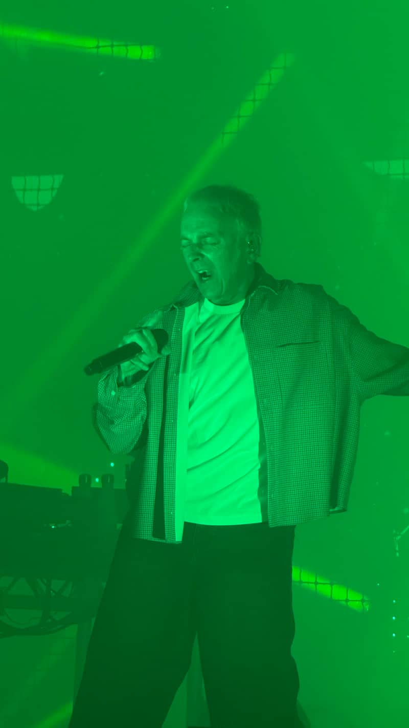Karl Hyde on stage singing Two Months Off surrounded by green light