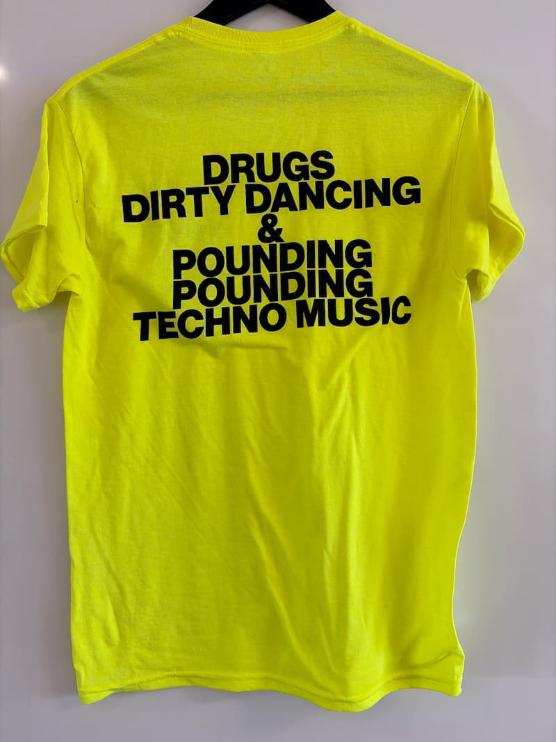 The back of a bright yellow t-shirt in black writing are the words: Drugs Dirty Dancing & Pounding Pounding Techno Music