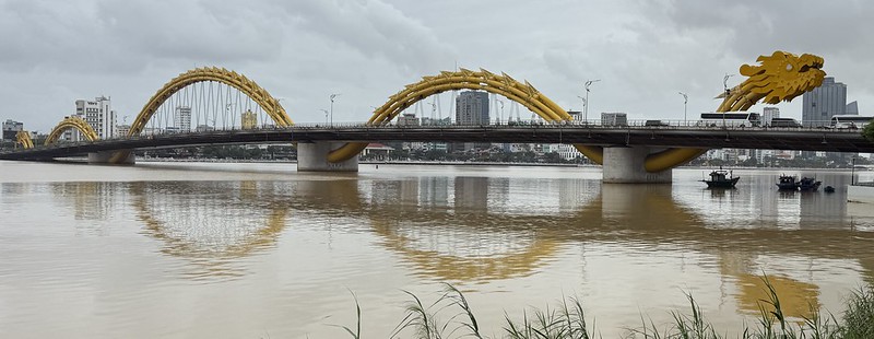 A panorama photo of the dragon bridge there is a golden dragon crossing the river, made into a road bridge. The body of the dragon is reflected in the river.