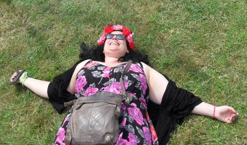Sarah lying collapsed in a field delighted to be at a music festival again, she is wearing a headband of red and pink flowers and a huge smile.