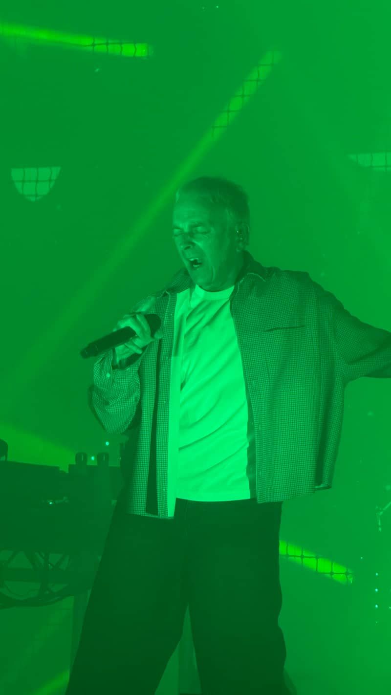 Karl Hyde on stage singing Two Months Off surrounded by green light