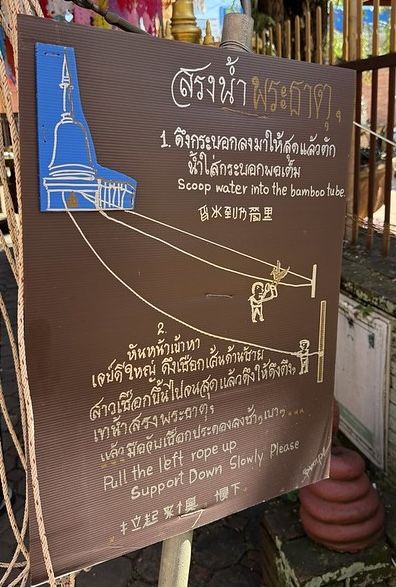 Instructions for the dragon hoist written in Thai and English - 1 scoop water into bamboo tube, 2 Pull left rope up, support down slowly please